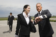 Photo: Pilot and a cabin crew checking the time with a businessman walking in the background Pilot and a cabin crew checking the time with a businessman walking in the background