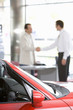 Photo: Salesman shaking hands with male customer in car showroom, focus on red convertible in foreground Salesman shaking hands with male customer in car showroom, focus on red convertible in foreground
