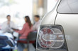 Photo: Salesman and couple sitting at desk in car showroom, focus on tail light in foreground Salesman and couple sitting at desk in car showroom, focus on tail light in foreground