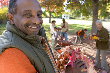 Photo: Multi-generational family collecting autumn leaves in garden, focus on grandfather standing in foreground, portrait Multi-generational family collecting autumn leaves in garden, focus on grandfather standing in foreground, portrait