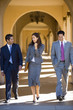 Photo: Businesswoman and two businessmen walking side by side in building arcade, laughing, front view Businesswoman and two businessmen walking side by side in building arcade, laughing, front view