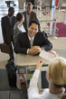 Photo: Businessman standing at airport check-in counter, smiling, female attendant looking at ticket, elevated view Businessman standing at airport check-in counter, smiling, female attendant looking at ticket, elevated view