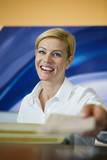 Photo: Female attendant passing ticket to customer at airport check-in counter, smiling, portrait (personal perspective) Female attendant passing ticket to customer at airport check-in counter, smiling, portrait (personal perspective)