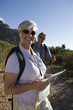 Photo: Mature couple hiking on mountain trail, woman standing in foreground, holding map, smiling, portrait Mature couple hiking on mountain trail, woman standing in foreground, holding map, smiling, portrait