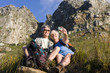 Photo: Mature couple sitting on mountain slope, woman taking self-portrait with digital camera, smiling, low angle view Mature couple sitting on mountain slope, woman taking self-portrait with digital camera, smiling, low angle view