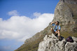 Photo: Mature man hiking on mountain trail, sitting on rock, looking at scenery, shielding eyes, side view Mature man hiking on mountain trail, sitting on rock, looking at scenery, shielding eyes, side view