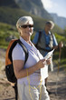 Photo: Mature couple, with rucksacks, hiking on mountain trail, focus on woman holding map and compass, smiling, portrait Mature couple, with rucksacks, hiking on mountain trail, focus on woman holding map and compass, smiling, portrait