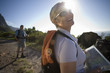 Photo: Mature couple, with rucksacks, hiking on mountain trail in bright sunlight, focus on woman holding map, smiling (lens flare) Mature couple, with rucksacks, hiking on mountain trail in bright sunlight, focus on woman holding map, smiling (lens flare)