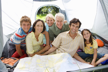 Photo: Multi-generational family sitting inside tent on camping trip, looking at map, smiling, portrait Multi-generational family sitting inside tent on camping trip, looking at map, smiling, portrait