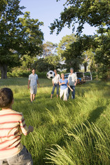 Photo: Multi-generational family playing with soccer ball in woodland clearing on camping trip Multi-generational family playing with soccer ball in woodland clearing on camping trip