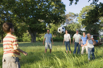 Photo: Multi-generational family playing with soccer ball in woodland clearing on camping trip Multi-generational family playing with soccer ball in woodland clearing on camping trip