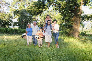 Photo: Multi-generational family walking in woodland clearing on camping trip, boy (8-10) holding soccer ball Multi-generational family walking in woodland clearing on camping trip, boy (8-10) holding soccer ball