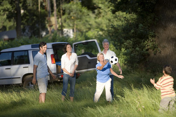 Photo: Multi-generational family playing with soccer ball in woodland clearing on camping trip Multi-generational family playing with soccer ball in woodland clearing on camping trip