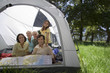 Photo: Multi-generational family relaxing inside tent in woodland clearing, smiling, portrait Multi-generational family relaxing inside tent in woodland clearing, smiling, portrait