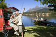 Photo: Boy (8-10) holding fishing rod from SUV with father and grandfather, rest of family standing on lake jetty beside boat Boy (8-10) holding fishing rod from SUV with father and grandfather, rest of family standing on lake jetty beside boat