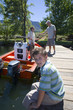 Photo: Boy (8-10) sitting on lake jetty, smiling, side view, portrait, father and grandfather loading fishing rods into motorboat Boy (8-10) sitting on lake jetty, smiling, side view, portrait, father and grandfather loading fishing rods into motorboat