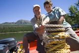 Photo: Grandfather and grandson (8-10) standing in motorboat beside lake jetty, tying rope to mooring post Grandfather and grandson (8-10) standing in motorboat beside lake jetty, tying rope to mooring post
