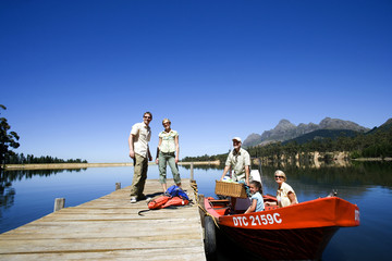 Photo: Multi-generational family loading motorboat with provisions at lake jetty, grandfather holding picnic hamper Multi-generational family loading motorboat with provisions at lake jetty, grandfather holding picnic hamper