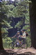 Photo: Young couple, with rucksacks, mountain biking along woodland trail beside lake, holding map, smiling, portrait Young couple, with rucksacks, mountain biking along woodland trail beside lake, holding map, smiling, portrait