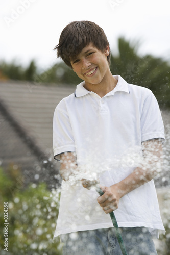 Photo: A young boy watering the garden with a hose A young boy watering the garden with a hose