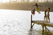 Photo: Father and son (8-10), in swimwear, jumping off jetty into lake at sunset, mother and daughter (7-9) cheering, rear view Father and son (8-10), in swimwear, jumping off jetty into lake at sunset, mother and daughter (7-9) cheering, rear view