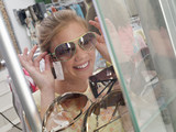 Photo: Teenage girl (14-16) trying on sunglasses from display rack in shop, smiling, close-up (tilt) Teenage girl (14-16) trying on sunglasses from display rack in shop, smiling, close-up (tilt)