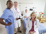 Photo: Doctors and nurse standing beside male patient lying in hospital bed, smiling, portrait Doctors and nurse standing beside male patient lying in hospital bed, smiling, portrait