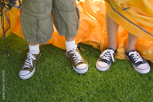 Photo: Brother and sister (8-10) assembling dome tent on garden lawn, standing beside orange outer tent canvas, low section, close-up, front view Brother and sister (8-10) assembling dome tent on garden lawn, standing beside orange outer tent canvas, low section, close-up, front view