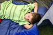 Photo: Boy (8-10) lying on sleeping bag in tent entrance, eyes closed, sleeping with hands behind head, side view Boy (8-10) lying on sleeping bag in tent entrance, eyes closed, sleeping with hands behind head, side view
