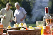 Two men talking in garden at family barbecue, focus on food and wine on table in foreground
