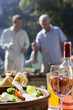 Two men talking in garden at family barbecue, focus on food and wine on table in foreground