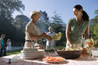 Photo: Senior woman passing corn cobs to adult daughter at family barbecue in garden, smiling Senior woman passing corn cobs to adult daughter at family barbecue in garden, smiling