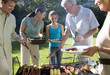 Photo: Three generation family standing beside barbecue grill in garden, senior man serving granddaughter (11-13) sausage, smiling Three generation family standing beside barbecue grill in garden, senior man serving granddaughter (11-13) sausage, smiling