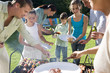 Photo: Three generation family standing beside barbecue grill in garden, adults serving children (8-13) food, smiling Three generation family standing beside barbecue grill in garden, adults serving children (8-13) food, smiling