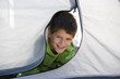 Boy (8-10) lying on front inside tent, poking head out of zipped entrance, smiling, front view, portrait