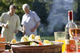 Photo: Two men talking in garden at family barbecue, focus on food and wine on table in foreground Two men talking in garden at family barbecue, focus on food and wine on table in foreground