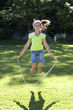 Photo: Girl (8-10) playing with skipping rope on garden lawn, smiling, front view, portrait Girl (8-10) playing with skipping rope on garden lawn, smiling, front view, portrait