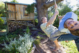 Photo: Father and son (8-10) swinging on garden rope swing near tree house, smiling, portrait (wide angle) Father and son (8-10) swinging on garden rope swing near tree house, smiling, portrait (wide angle)