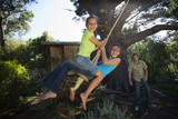 Photo: Two girls (8-13) swinging on garden rope swing near tree house, father pushing in background, smiling, portrait Two girls (8-13) swinging on garden rope swing near tree house, father pushing in background, smiling, portrait