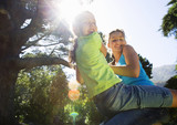 Photo: Two girls (8-13) swinging on garden rope swing, smiling, portrait, low angle view (lens flare) Two girls (8-13) swinging on garden rope swing, smiling, portrait, low angle view (lens flare)