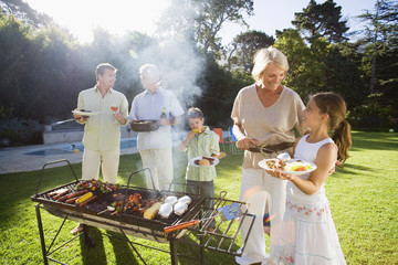Photo: Family having barbecue in summer garden, senior woman serving granddaughter (8-10) beside grill, smiling (lens flare) Family having barbecue in summer garden, senior woman serving granddaughter (8-10) beside grill, smiling (lens flare)