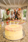 Photo: Parents and grandparents celebrating birthday at home, smiling, portrait, birthday cake on table in foreground Parents and grandparents celebrating birthday at home, smiling, portrait, birthday cake on table in foreground