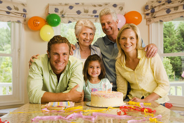 Photo: Three generation family celebrating birthday at home, girl (4-6) sitting beside birthday cake, smiling, portrait Three generation family celebrating birthday at home, girl (4-6) sitting beside birthday cake, smiling, portrait