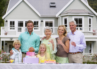 Photo: Three generation family celebrating birthday in summer garden in front of house, smiling, portrait Three generation family celebrating birthday in summer garden in front of house, smiling, portrait