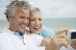 Foto: A senior couple on a beach taking a picture with a digital camera A senior couple on a beach taking a picture with a digital camera