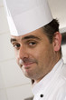 Photo: Male chef standing in commercial kitchen, smiling, close-up, side view, portrait (tilt) Male chef standing in commercial kitchen, smiling, close-up, side view, portrait (tilt)