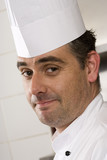Photo: Male chef standing in commercial kitchen, smiling, close-up, side view, portrait (tilt) Male chef standing in commercial kitchen, smiling, close-up, side view, portrait (tilt)