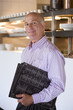 Photo: Male restaurant manager standing in commercial kitchen, carrying menus, smiling, side view, portrait Male restaurant manager standing in commercial kitchen, carrying menus, smiling, side view, portrait