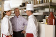 Photo: Restaurant manager talking to male and female chefs in commercial kitchen, smiling Restaurant manager talking to male and female chefs in commercial kitchen, smiling