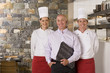 Photo: Restaurant manager standing with male and female chefs near commercial kitchen, smiling, front view, portrait Restaurant manager standing with male and female chefs near commercial kitchen, smiling, front view, portrait